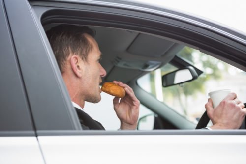 Businessman having coffee and doughnut on the phone in his car